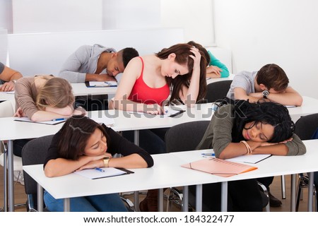 Bored female college student with classmates sleeping at desk in classroom