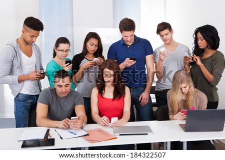 Group of multiethnic university students using mobile phones at desk in classroom