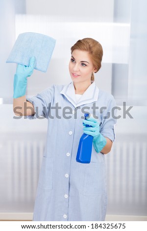 Portrait Of Happy Young Maid Cleaning Glass With Sponge