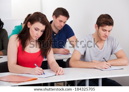 Young college students writing at desk in classroom