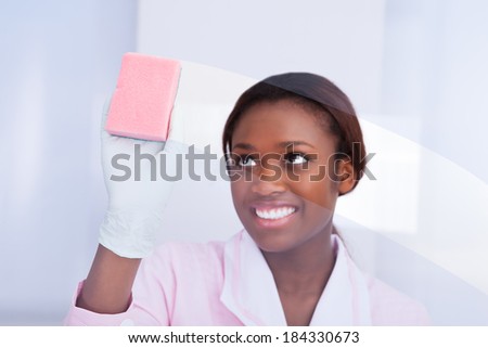 Happy African American female housekeeper cleaning glass in hotel