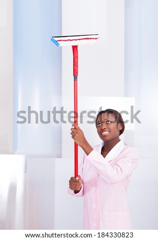 Smiling African American housekeeper cleaning glass in hotel
