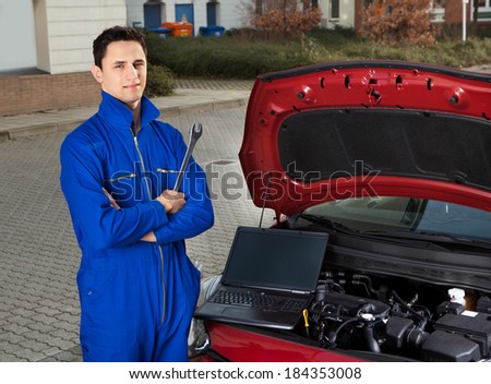 Portrait of confident mechanic with arms crossed holding wrench by car on street