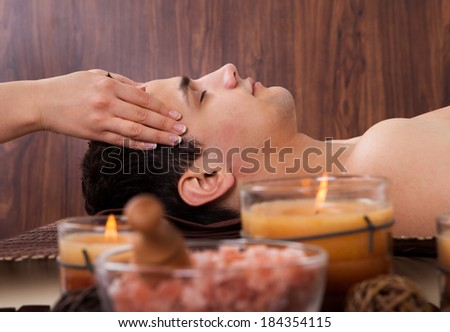Side view of young man receiving head massage from massager in spa