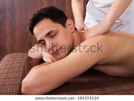 Relaxed young man with eyes closed receiving shoulder massage in spa