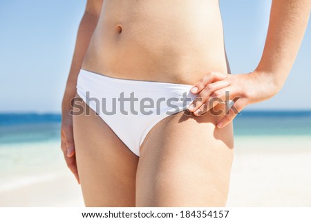 Midsection of woman in bikini with hand on hip standing on beach