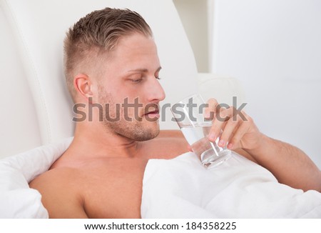 Man lying in bed propped up against the pillows drinking a glass of fresh water
