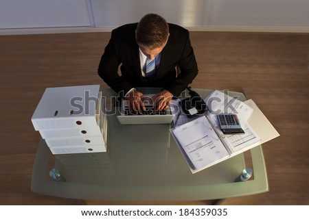 Businessman under pressure working overtime late into the evening sitting at his desk collating a report for a deadline in the morning