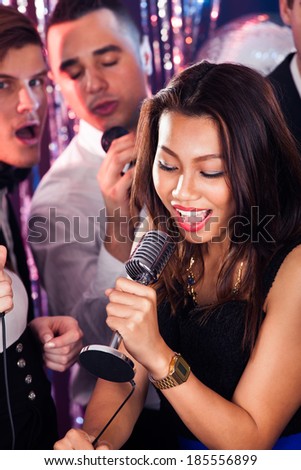 Young woman singing into microphone with friends in background at karaoke party