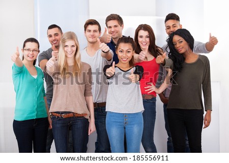 Group portrait of confident multiethnic college students gesturing thumbs up in classroom