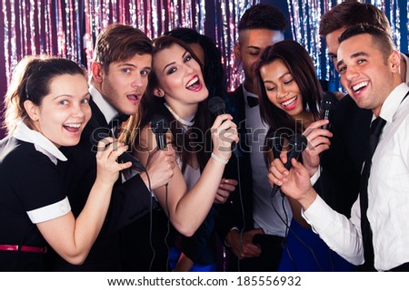 Portrait of happy multiethnic friends singing into microphones at karaoke party