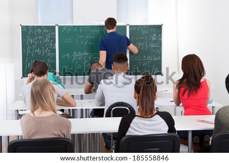 Rear view of teacher teaching mathematics to university students in classroom