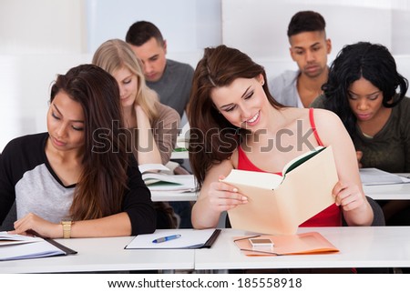 Happy female college students studying at desk in classroom