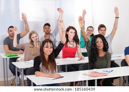 Portrait of college students raising hands while sitting in classroom
