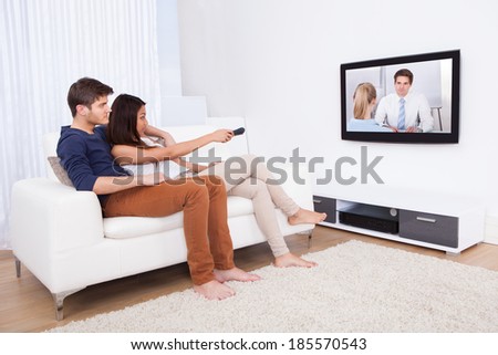 Young couple watching TV while sitting on sofa in living room at home