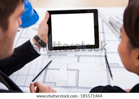 Cropped image of architects with digital tablet working on blueprint at desk in office