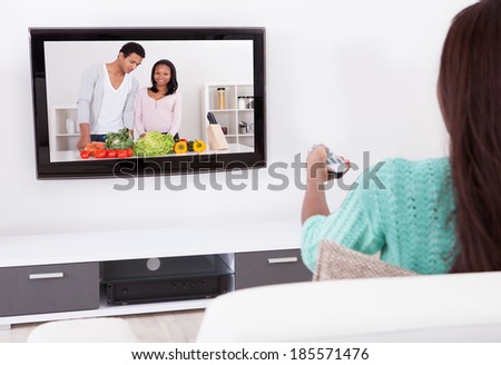 Side view of young woman watching TV in living room