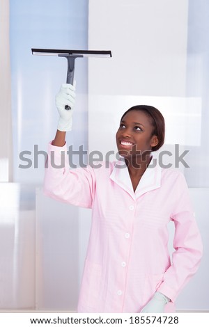 Smiling African American housekeeper cleaning glass in hotel