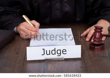 Cropped image of judge writing on legal documents at desk