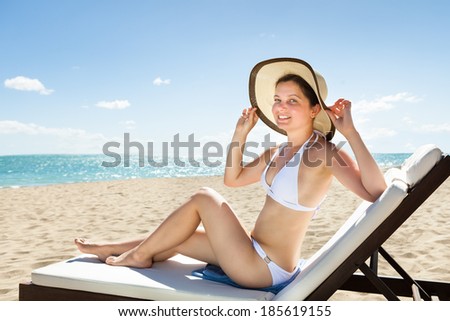 Portrait of attractive young woman in bikini relaxing on deck chair at beach