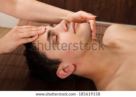 Side view of young man receiving head massage from massager in spa