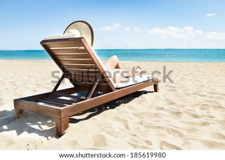 Side view of young woman in bikini sunbathing on deck chair at beach