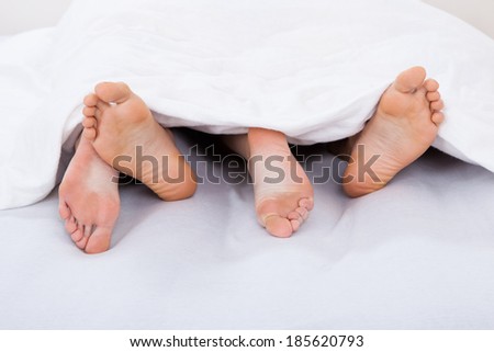 Low section of intimate couple under blanket on mattress at home
