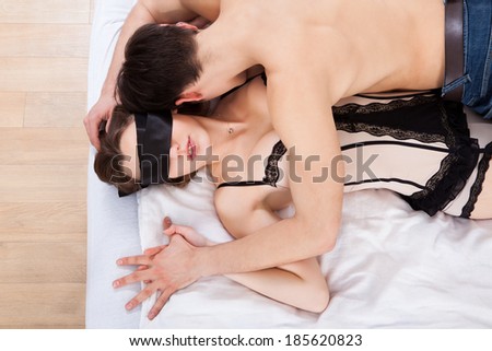 Side view of young man kissing sexy blindfolded woman in bed at home