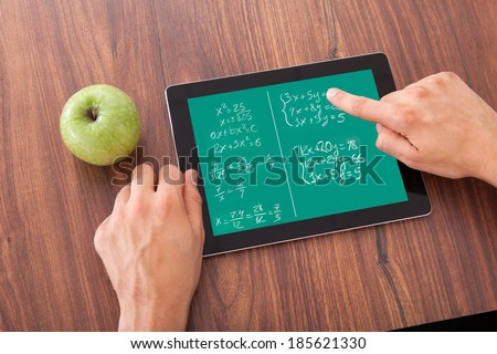 Cropped image of young male student solving math\'s problem on digital tablet by green apple on table
