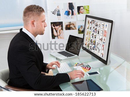 Businessman sitting at his desk in front of a large screen monitor editing photographs