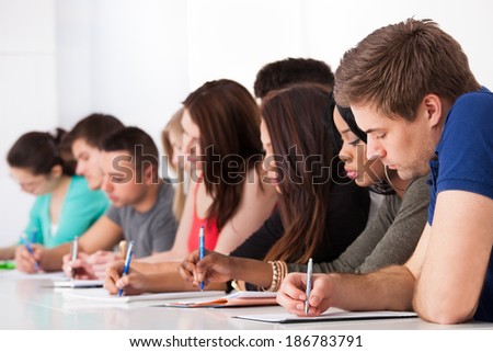 Row of multiethnic college students writing at desk in classroom