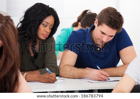 Portrait of male college student sitting at desk with classmates in background
