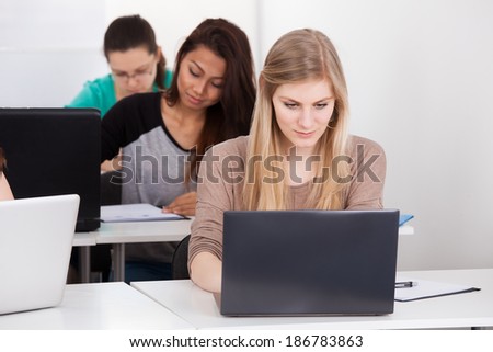 Portrait of beautiful university student sitting with laptop at desk in classroom