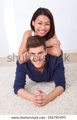 Portrait of loving woman embracing man from behind while lying on rug at home