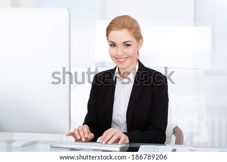 Young Smiling Businesswoman Using Computer At Office Desk