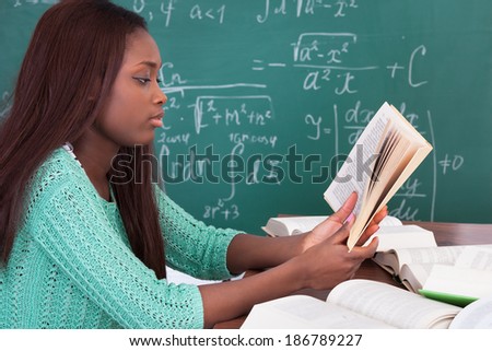 Side view of African American teacher reading book at classroom desk