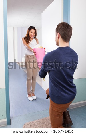 Young man giving bouquet to happy woman while kneeling at house doorway