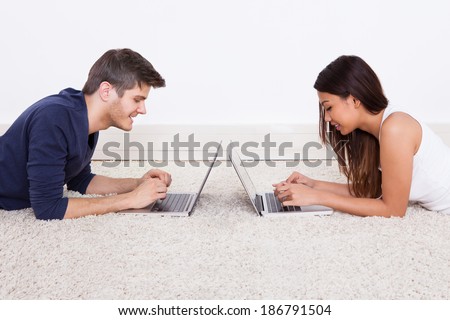 Side view of young couple using laptops while lying on rug at home