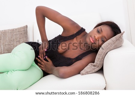 Young African American woman suffering from stomachache lying on sofa at home