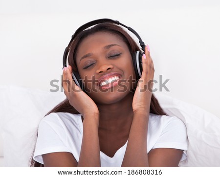 Happy African American woman enjoying music through headphones in bed at home