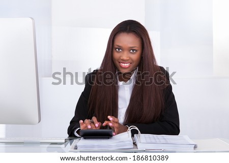 Portrait of confident businesswoman calculating tax at desk in office