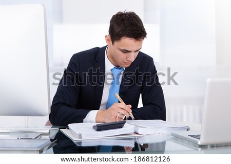 Young businessman computing tax at desk in office