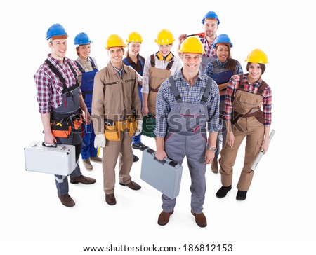 Large team of diverse artisans standing grouped together with their tools and hardhats lead by a handsome smiling foreman high angle isolated on white