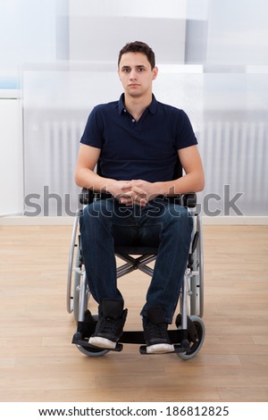 Full length portrait of young handicapped man sitting on wheelchair at home