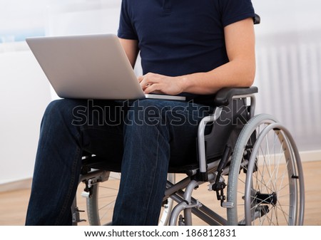 Cropped image of young handicapped man using laptop while sitting on wheelchair at home