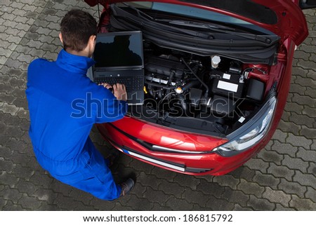 Side view of young mechanic using laptop while repairing car on street