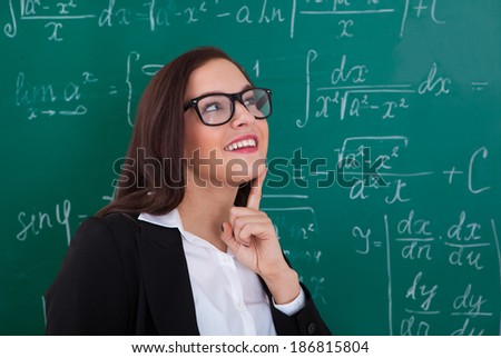Thoughtful young teacher looking at chalkboard in classroom