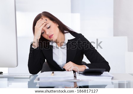 Tensed young businesswoman calculating tax at desk in office