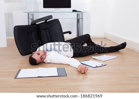 Full length of young businessman fallen from office chair