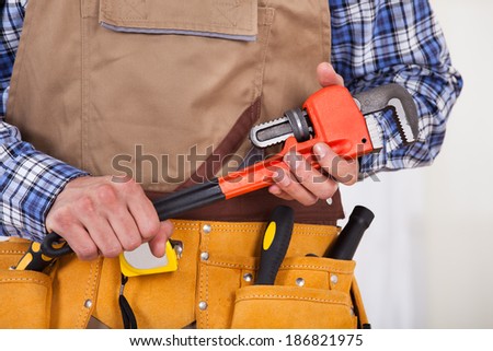Midsection of male repairman with tool belt holding pipe wrench